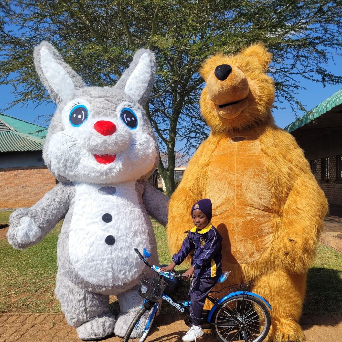 Mascots posing with a child on his bicycle at an outdoor party